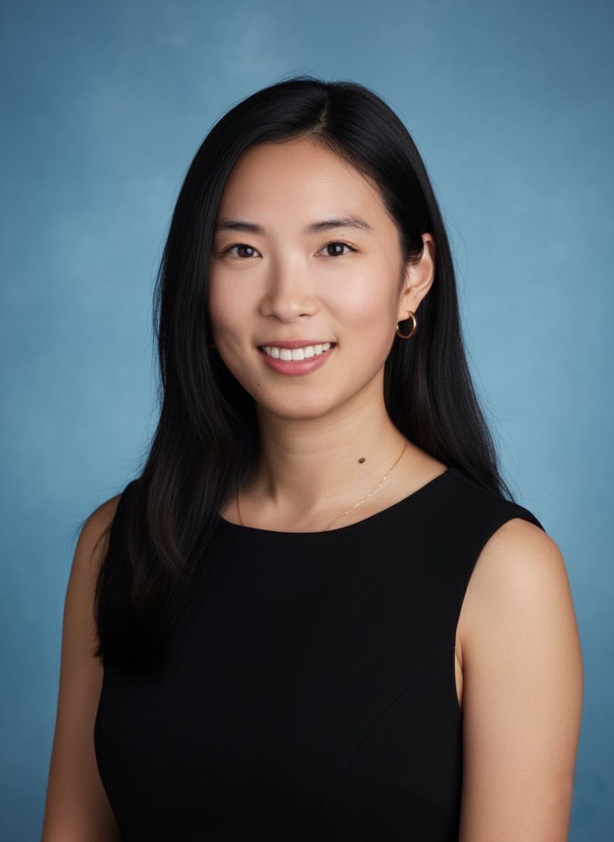 A doctoral student with long black hair and a black top smiles against a light blue background.