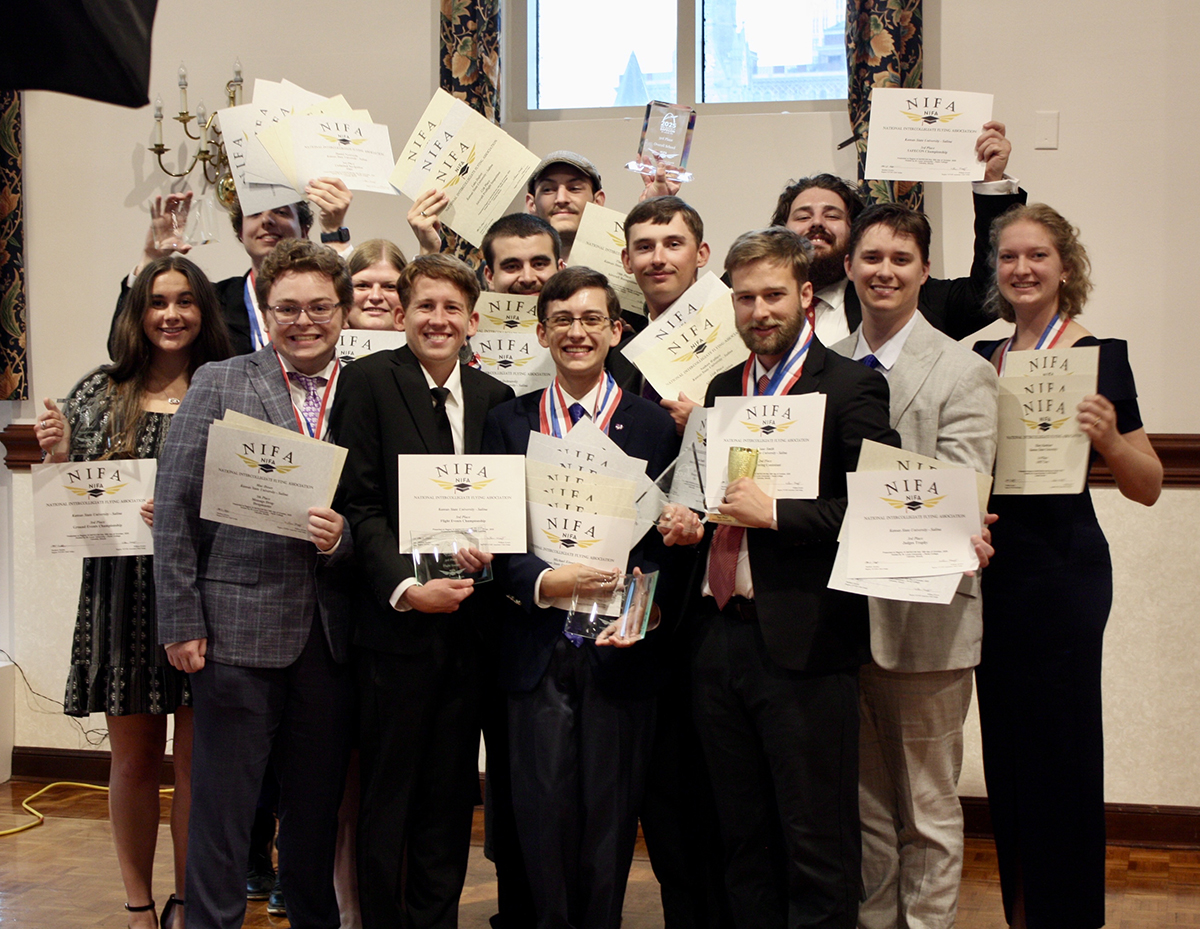 A group of students in professional attire standing in three rows hold up certificates, trophies and awards that say NIFA.
