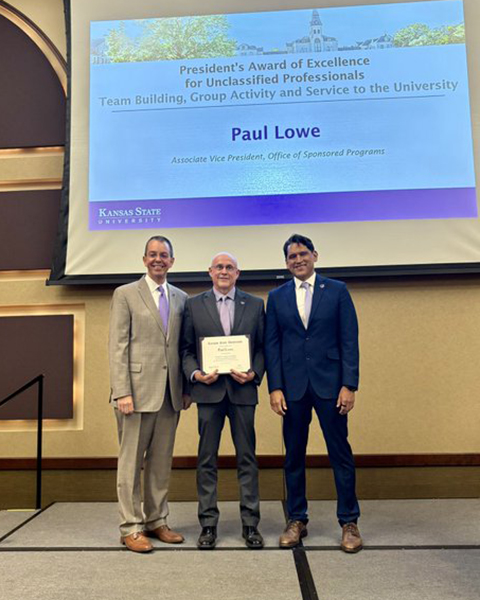 Paul Lowe receives an award from two university administrators standing on a stage.