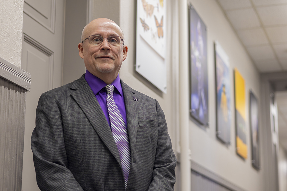 Paul Lowe poses for a portrait in a long hallway in a research office.